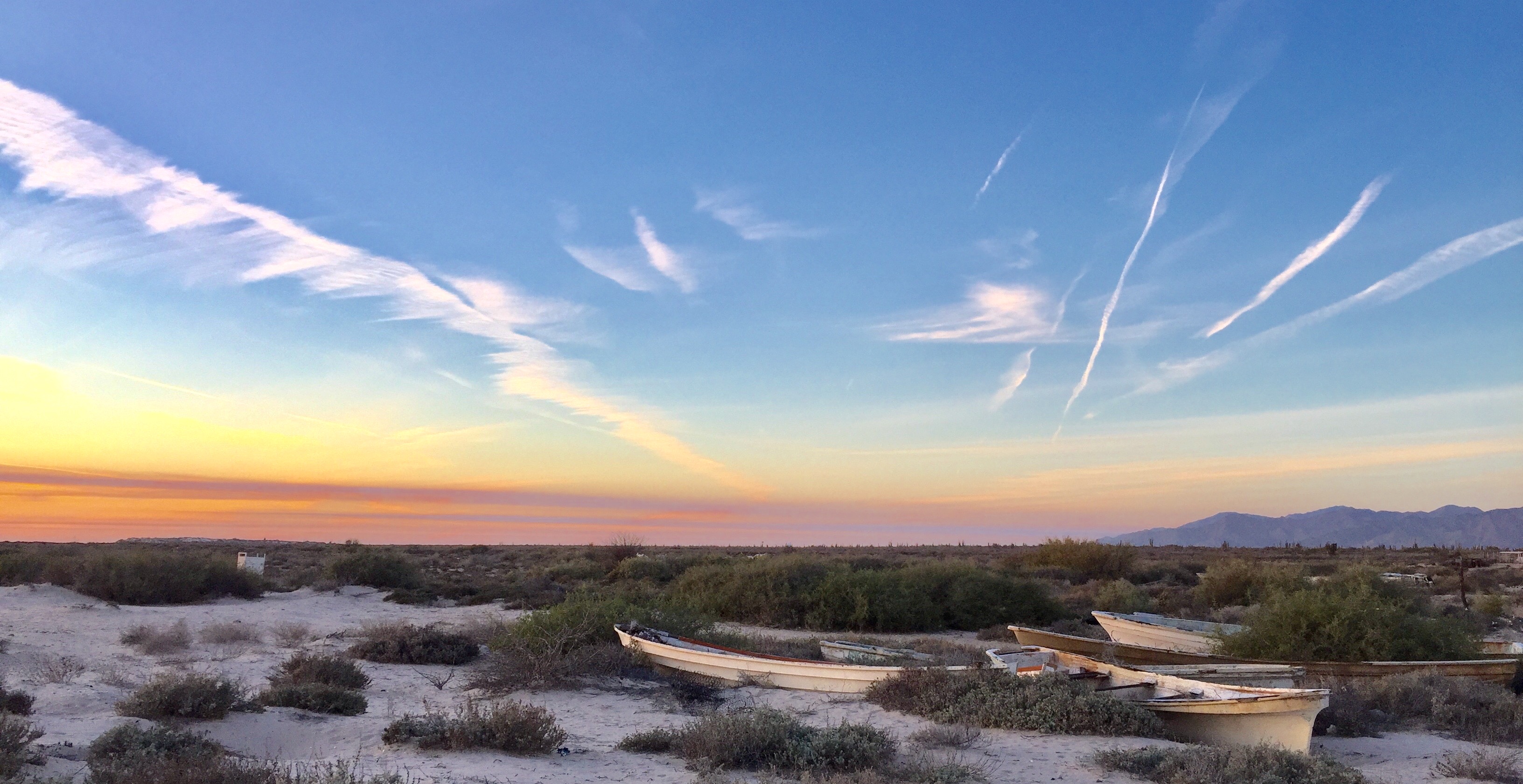 Una pequeña lancha de madera en la arena frente a un cielo con nubes cirros en tonos rosados
